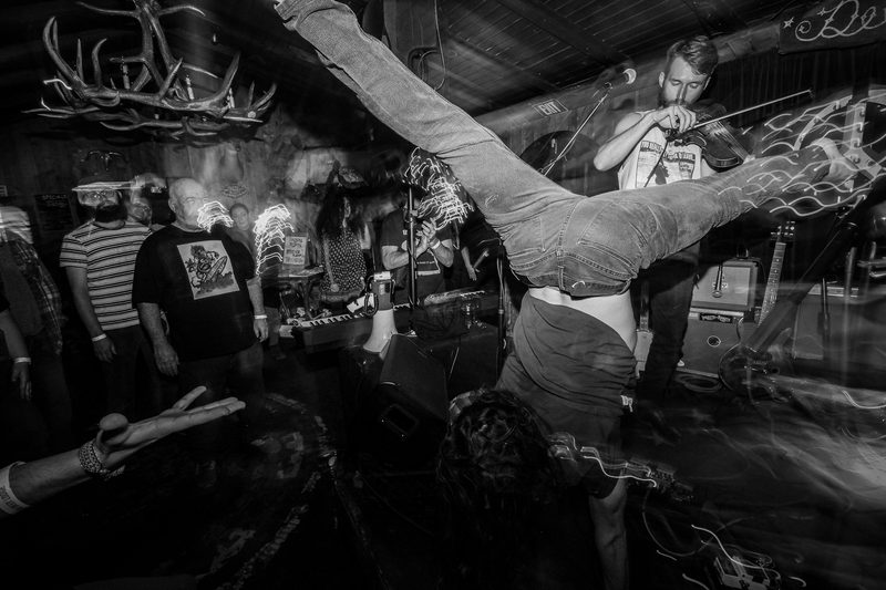 Black and white photo of a performer kicking his legs overhead above a packed crowd during an Insects vs. Robots show