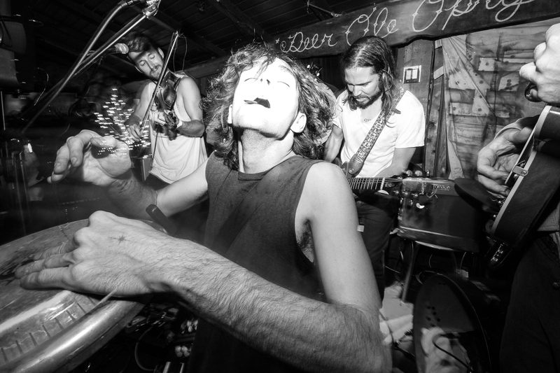 Black and white photo of a singer with his head tilted back mid-song while bandmates play behind him during an Insects vs. Robots show