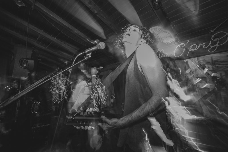 Black and white photo of a singer at the microphone with an arm raised during an Insects vs. Robots show