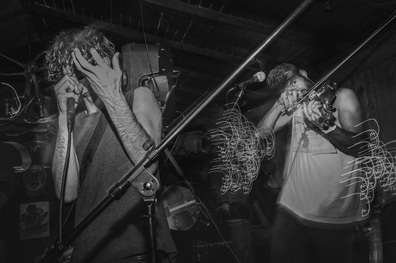 Black and white photo of two performers sharing microphones on stage during an Insects vs. Robots show