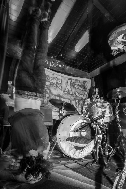 Black and white photo of a performer upside down while the drummer plays behind during an Insects vs. Robots show