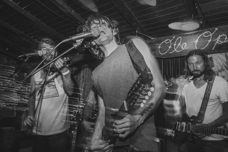 Black and white photo of a vocalist and bandmates performing together on a small stage during an Insects vs. Robots show
